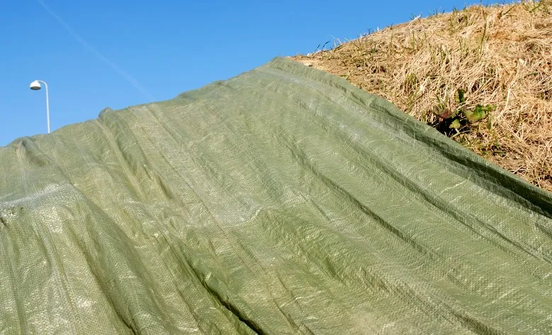 Lona verde de protección tensada cubriendo material apilado al aire libre