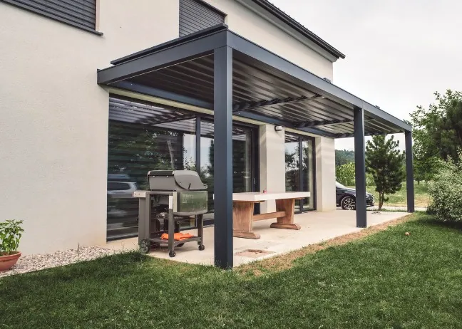 Pérgola bioclimática antracita adosada a la vivienda con comedor exterior y jardín