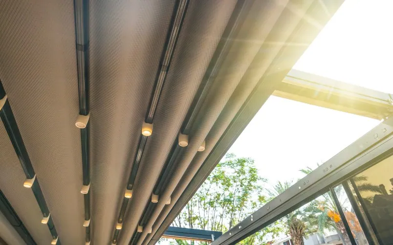 Palillería motorizada en una pérgola de aluminio Lona de palillería gris recogida bajo una pérgola de aluminio con focos integrados en la estructura