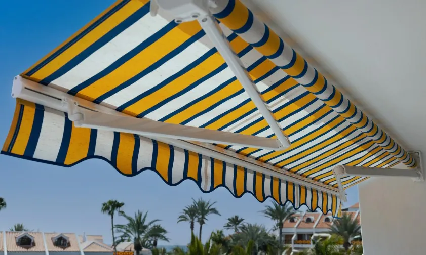 Toldo extensible de brazos articulados con lona a rayas azules y amarillas sobre una terraza