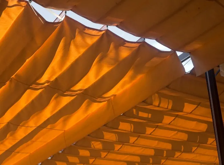 Lona de palillería naranja en ondas Lona naranja de palillería formando ondas sobre los perfiles transversales de una pérgola