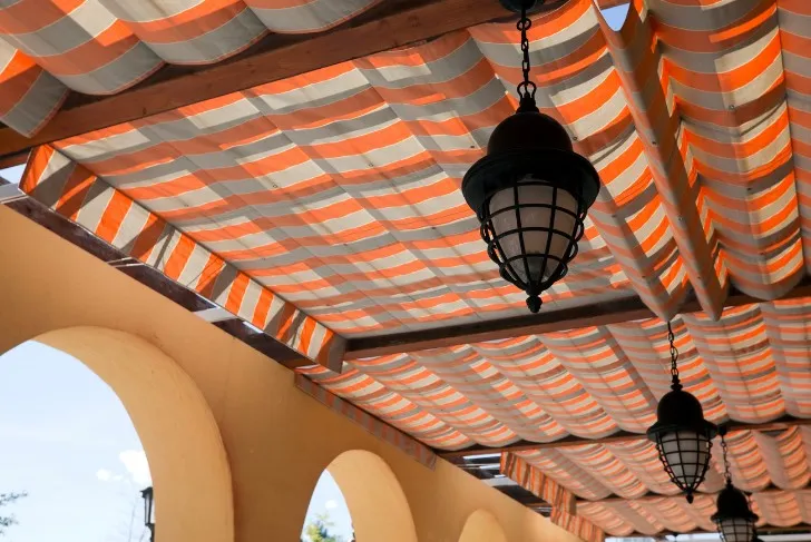 Lona de palillería a rayas naranjas y blancas recogida en pliegues bajo un porche con arcos y farolas