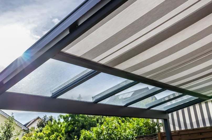 Toldo corredero de rayas bajo el techo de cristal de una pérgola de aluminio
