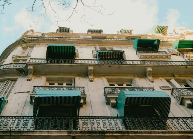 Toldos verdes de brazos, todos iguales, en los balcones de una fachada clásica