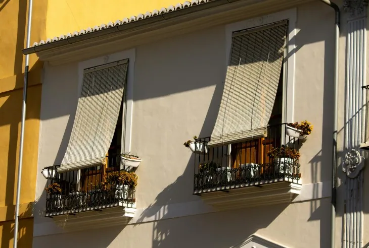 Toldos verticales de tejido microperforado bajados en las ventanas de una fachada amarilla